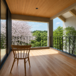 Wooden chair on a sunlit balcony with glass doors, overlooking blooming cherry trees and green foliage outside the railing.