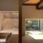 Sunlit modern interior with large windows and vertical wooden blinds casting striped shadows on a wooden floor and built-in bench area.