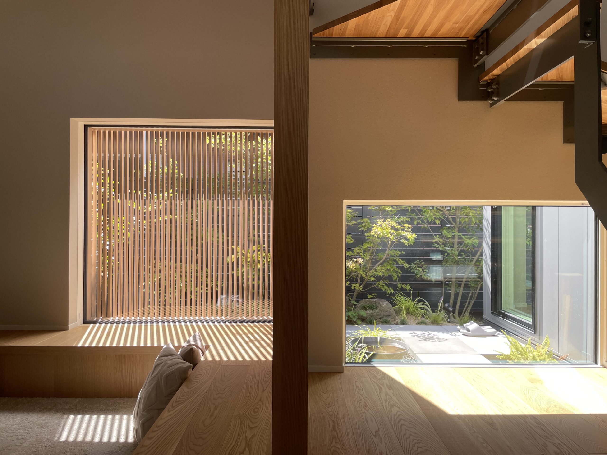 Sunlit modern interior with large windows and vertical wooden blinds casting striped shadows on a wooden floor and built-in bench area.