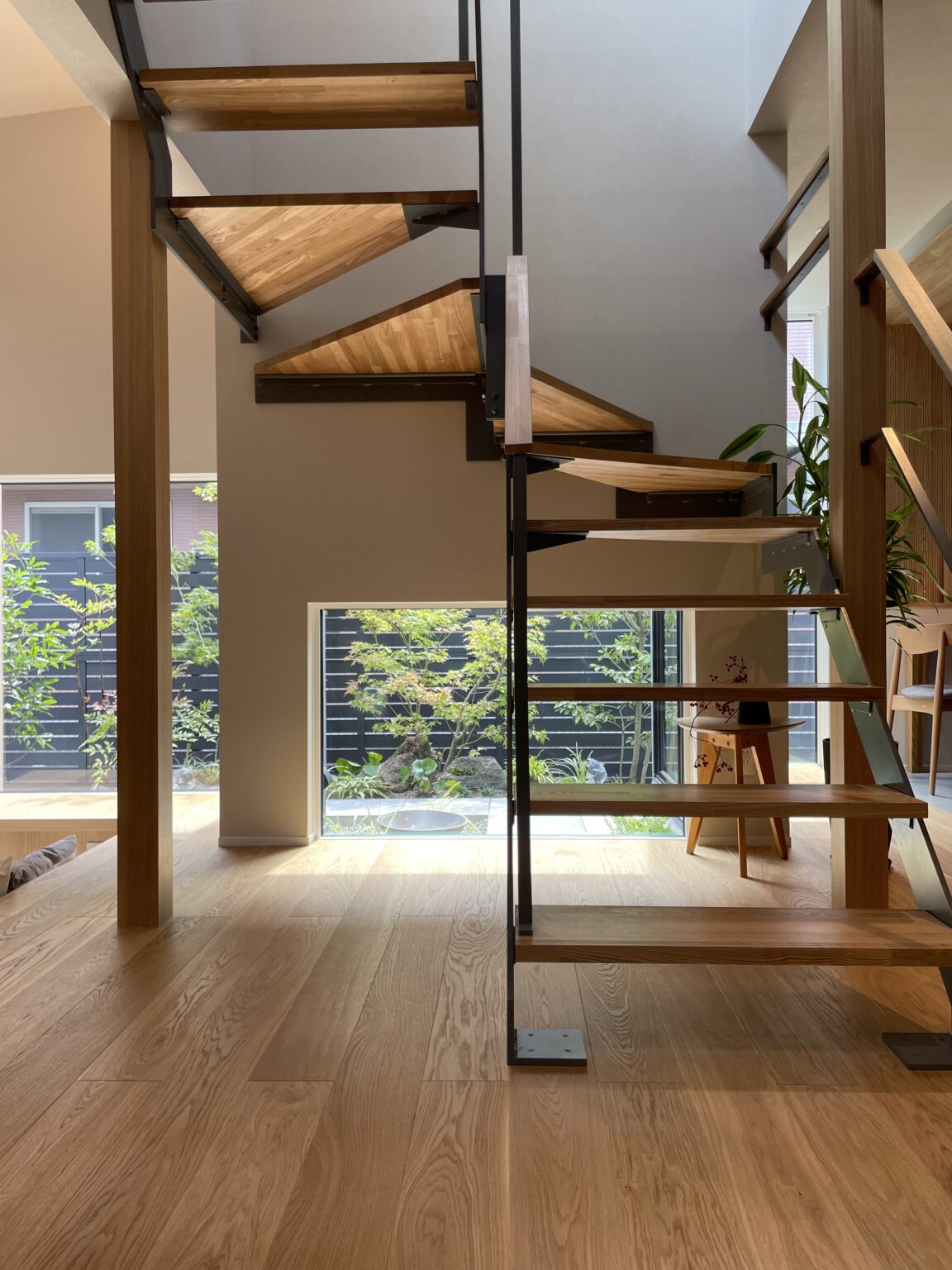 Modern open-riser staircase with wooden treads and black metal frame, ascending beside a glass wall and indoor plants.