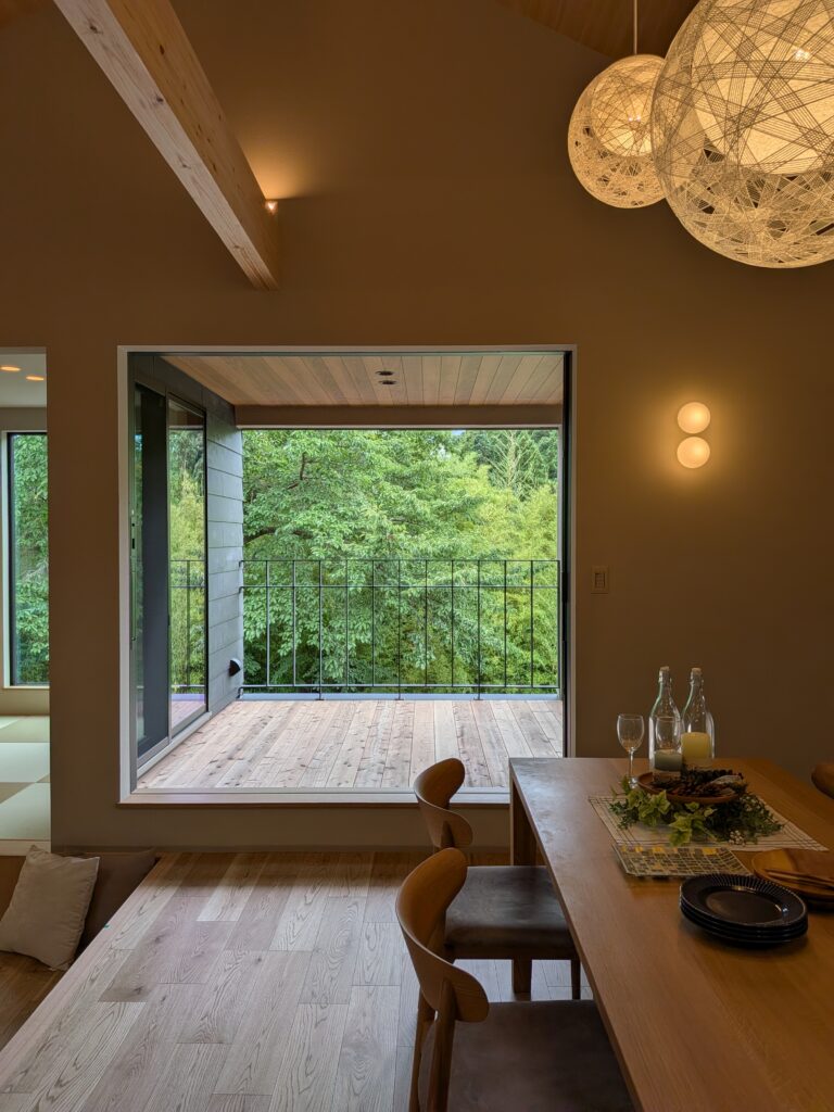 Open dining area with a large doorway to a wooden deck and lush green trees outside, warm ambient lighting.